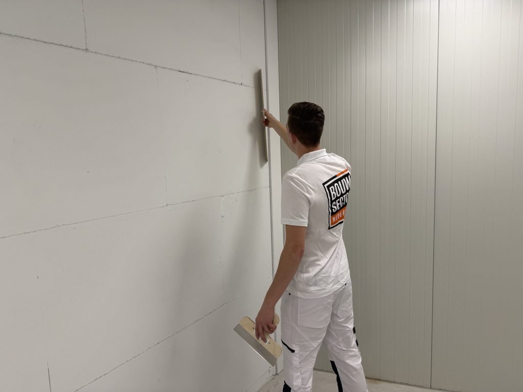 Stukadoor staat schuin voor een wand van kalkzandsteenblokken en controleert met de rei of de muur vlak is