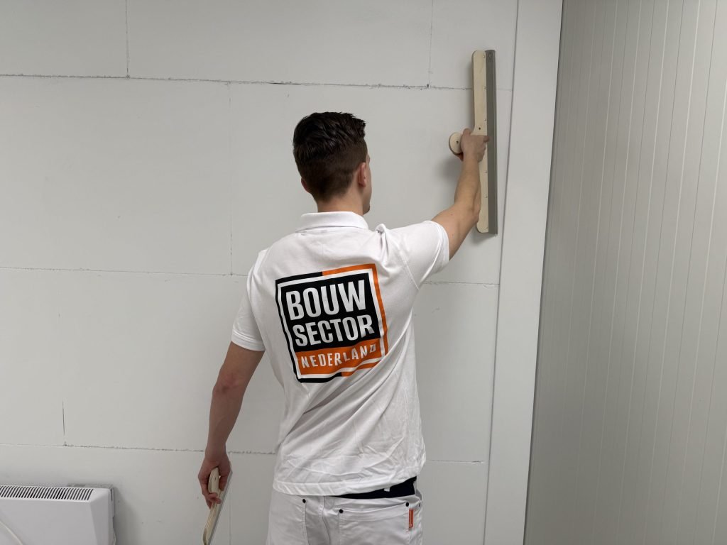 Stukadoor met het logo van Bouwsector Nederland op zijn rug trekt een wand vlak met een houten rei